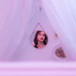 Artistic shot of a woman reflecting in a triangle mirror surrounded by soft drapery.